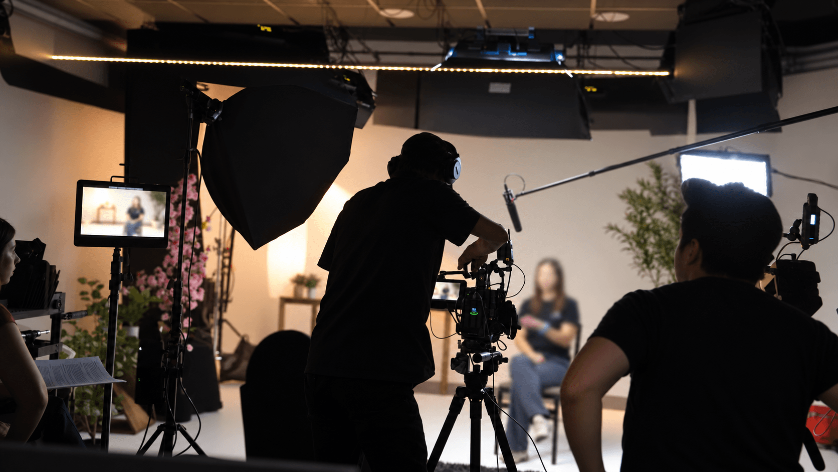 Behind the scenes of a studio interview, with the camera crew in the foreground and the interview subject softly out of focus.